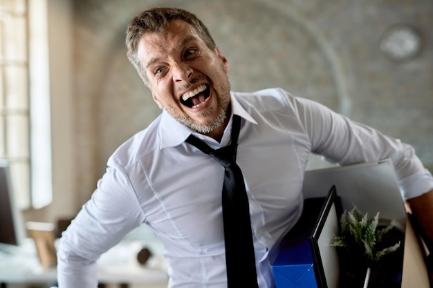 Fired businessman holding his belongings and screaming from frustration in the office