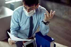 Free photo fired businessman wearing face mask and feeling frustrated while reading a notice in the office