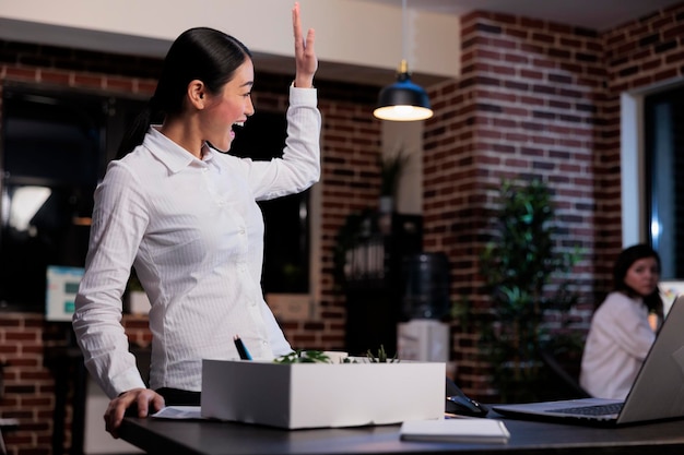 Fired businesswoman packing personal belongings while waving goodbye to office colleague. Dismissed business company employee putting personal stuff in cardboard box because of project failure.