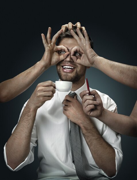 But first dinner. A male model surrounded by hands on dark wall. A young man has time for everything in his life, multitasking like a superhero. Concept of time managment, office work.