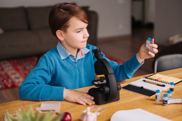 현미경을 사용하여 집에서 공부하는 1 학년 소년