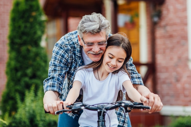 Free photo first lessons bicycle riding. handsome grandather teach his granddaughter to ride a bike. practicing near home.