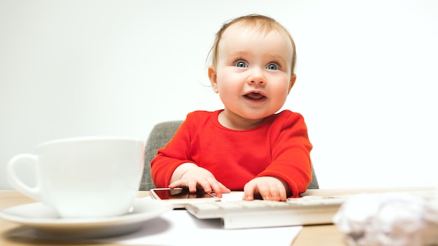 Первое смс. Ребенок девочка сидит с клавиатурой современного компьютера или ноутбука в белой студии