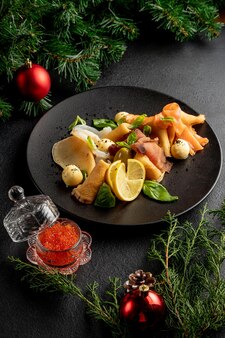 Рыбное блюдо на черной тарелке с красной икрой на темном рождественском фоне с елочными игрушками и еловыми ветками