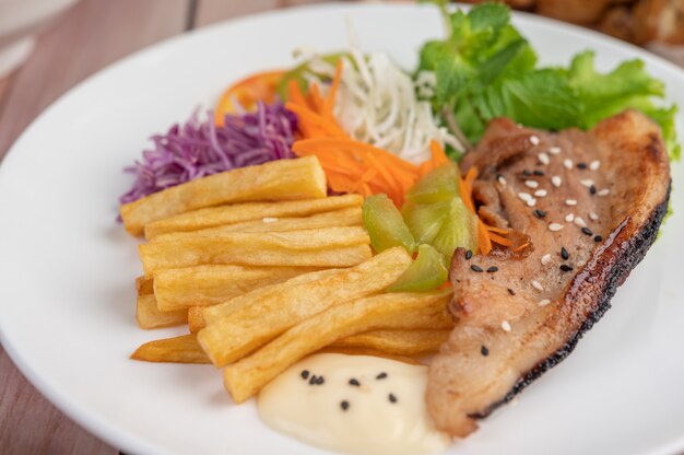 Fish steak with french fries, kiwi, lettuce, carrots, tomatoes, and cabbage in a white dish.