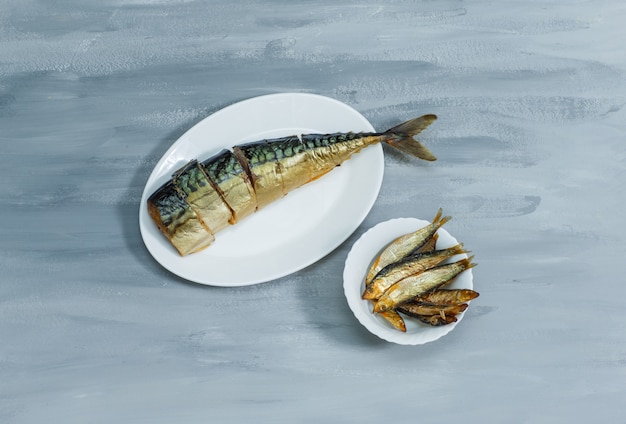 Рыба с ломтиками в белых тарелках на серой штукатурной поверхности