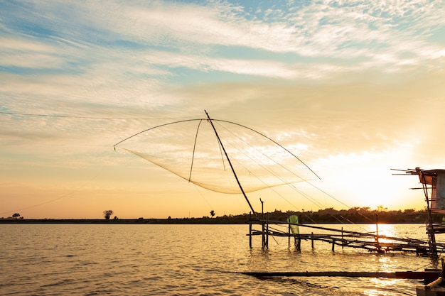 Инструменты рыболова в озере на небе захода солнца.