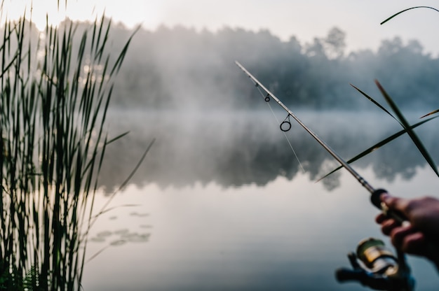 Рыбак с удочкой, спиннингом на берегу реки. туман на фоне озера. Premium Фотографии