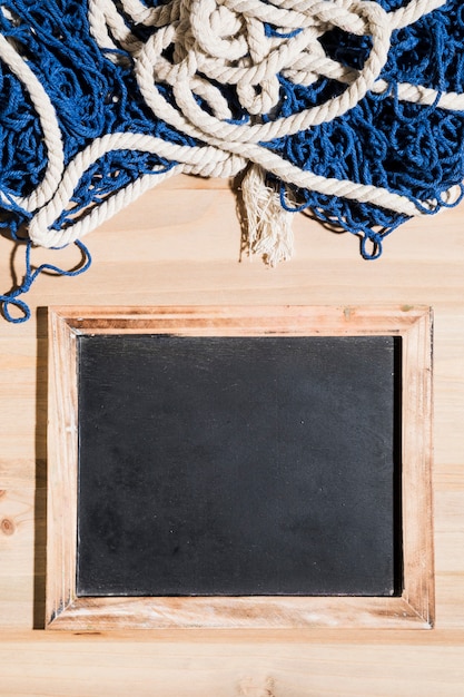 Fishing net over the blank blackboard over the wooden surface