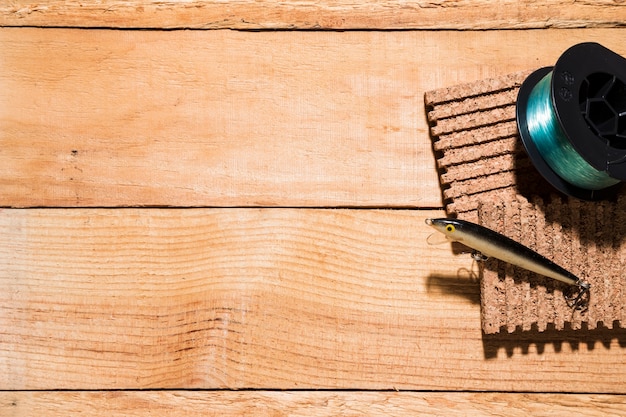 Fishing reel and lure on corkboard on wooden desk