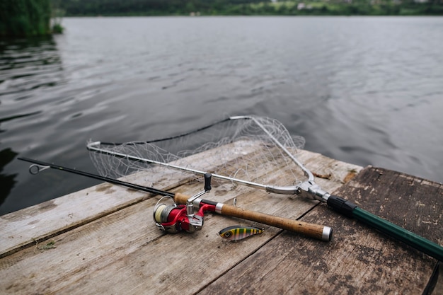 Fishing rod with lure and net on wooden pier over idyllic lake