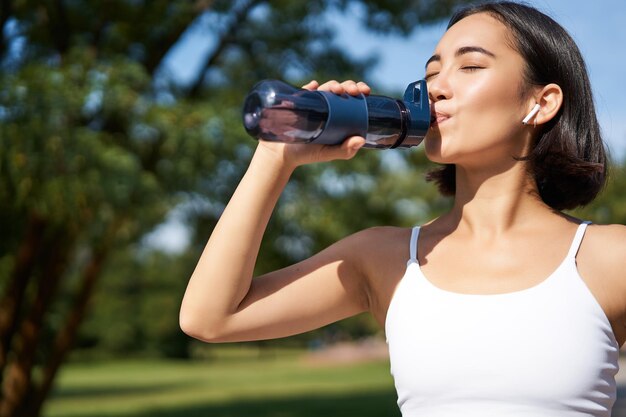 Free photo fit asian sportswoman drinks water while running marathon fitness girl jogging in park staying hydra