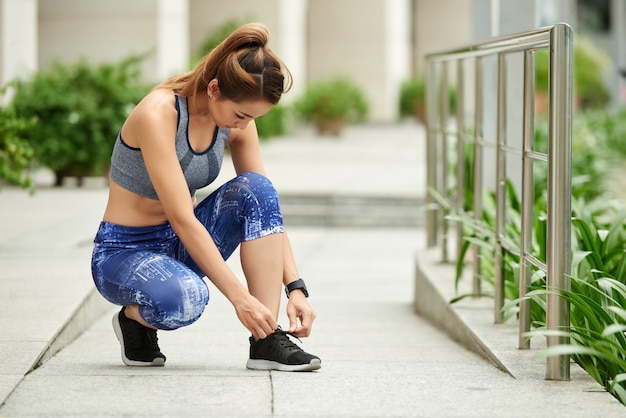 Donna asiatica adatta in abiti sportivi che lega i laccetti in via