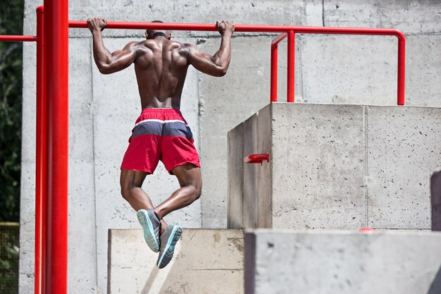 The fit athlete doing exercises. Afro or african american man outdoor at city. Pull up sport exercises. 