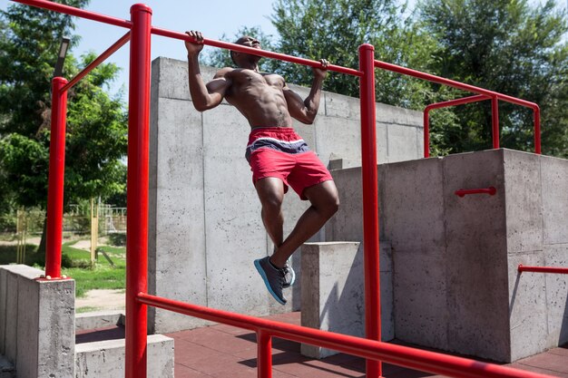 The fit athlete doing exercises at stadium. Afro or african american man outdoor at city. Pull up sport exercises. fitness, health, lifestyle concept