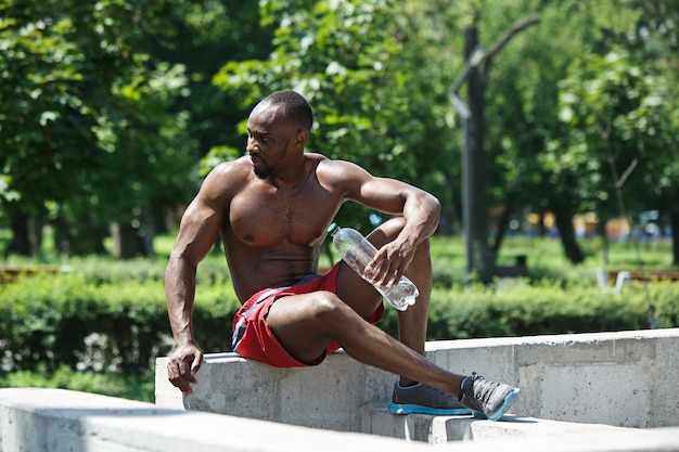 Free photo fit athlete resting and drinking water after exercises at stadium