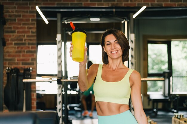 Fit caucasian beautiful woman in fitting sport wear at gym holds protein shaker