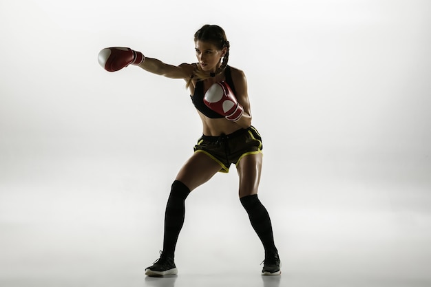 Fit caucasian woman in sportswear boxing isolated on white  wall. Novice female caucasian boxer training and practicing in motion and action. Sport, healthy lifestyle, movement concept.