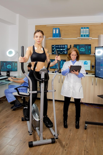 Free photo fit female testing stepper and doctor making notes in tablet. test with electrodes