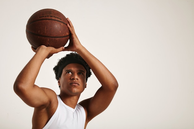 Free photo fit focused african american player with a short afro in white sleeveless shirt preparing to throw an old leather basketball