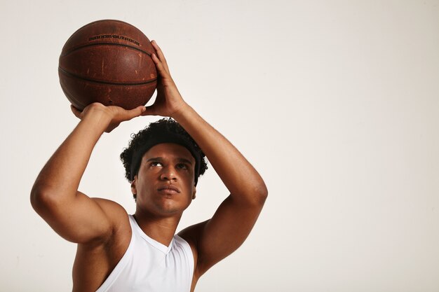 fit focused African American player with a short afro in white sleeveless shirt preparing to throw an old leather basketball