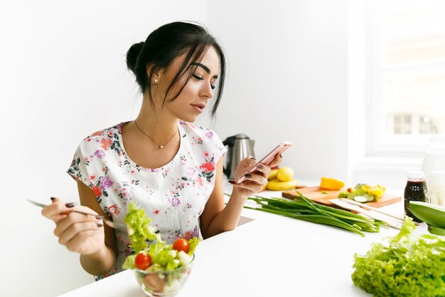 フィットの少女は彼女の電話をチェックし、台所でサラダを食べる