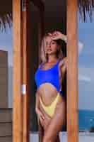 Foto gratuita montare una bella donna europea del corpo sportivo in bikini blu giallo alla moda in vacanza in un lussuoso hotel villa in stile bali, luce naturale, all'aperto. parete in legno.