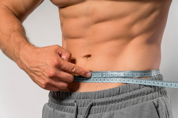 Fit man holding measuring tape around waist