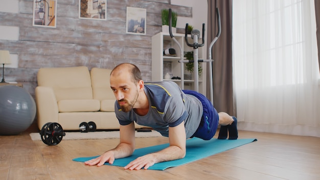 Fit man in sportswear doing plank workout on yoga mat at home.