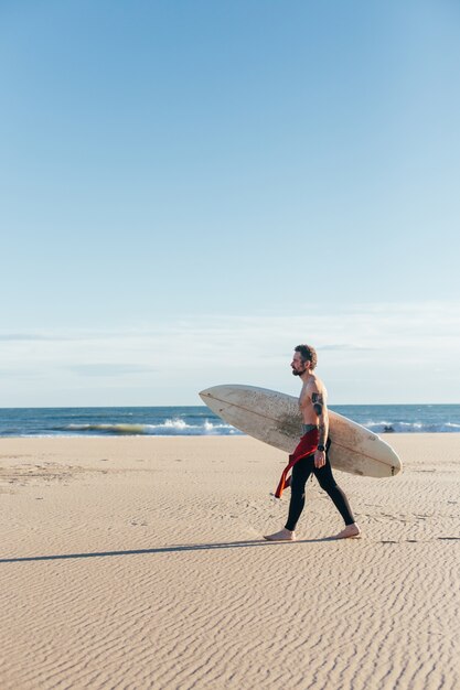 暖かい夏の日に空のビーチでサーフボードと中年の男性をフィットさせます