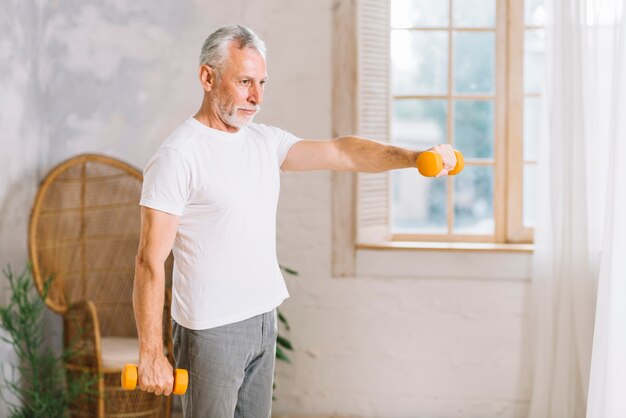 Fit senior man exercising with an orange dumbbells at home