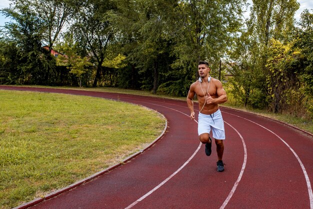 Fit shirtless man with white shorts and headphones around his neck running on a track