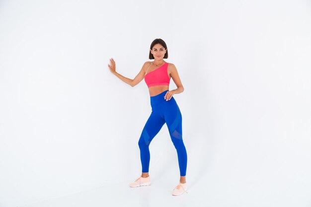 Fit tanned sporty woman with abs, fitness curves, wearing top and blue leggings on white