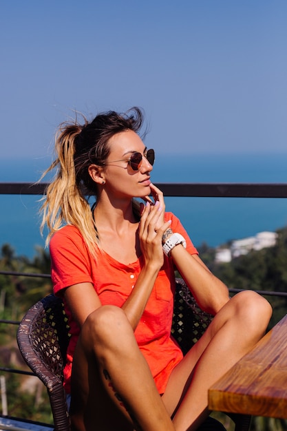 Fit tanned tattooed caucasian european woman with sport body and abs, in jean shorts and red orange shirt