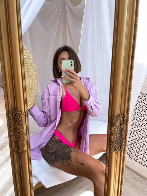 Fit tanned woman with perfect body takes photo selfie on phone in mirror at home