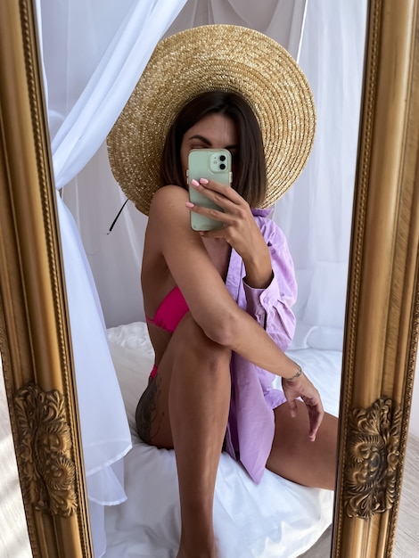 Fit tanned woman with perfect body takes photo selfie on phone in mirror at home