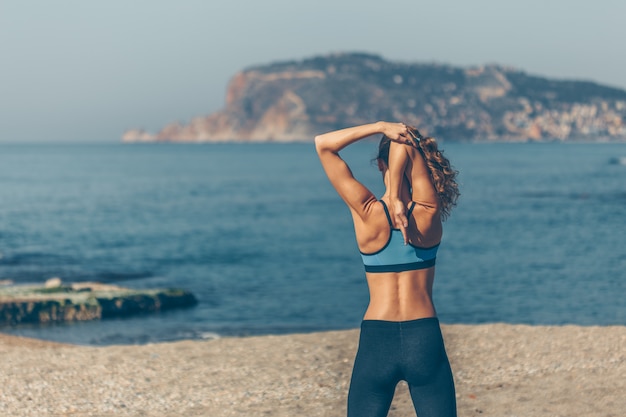 Free photo fit woman in fitness clothing doing warm-up exercise in beach during daytime with sea