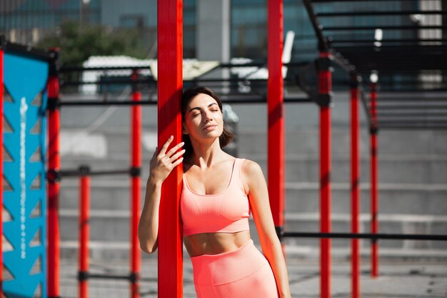 Fit woman in pink fitting sportswear outdoor at city sport square at sunny day