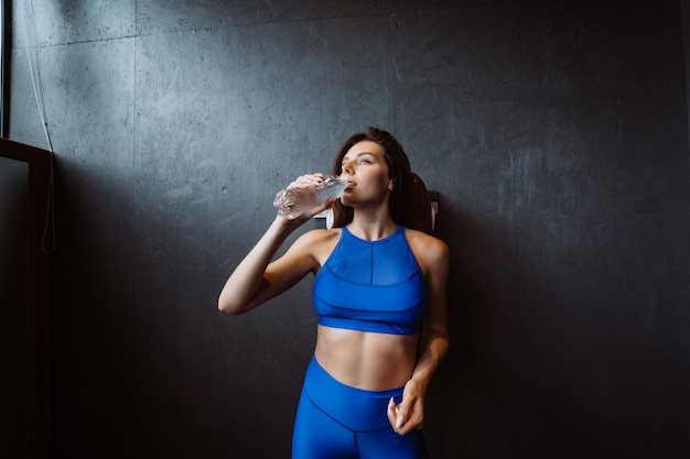 Fit woman posing on the camera. Girl drinks water from a bottle. Beauty of modern sport.