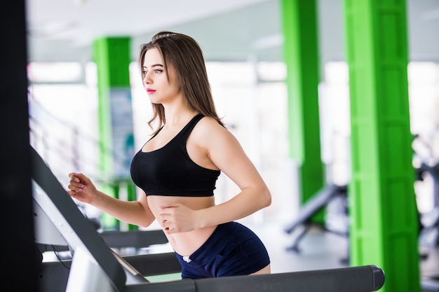 Fit woman runs on sport simulator in modern fitness centre dressed up in black sportswear