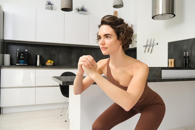 Подтянутая женщина в спортивной одежде делает упражнения на корточках дома, физические упражнения в помещении