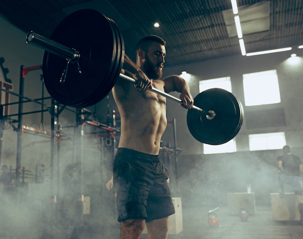 Fit young man lifting barbells working out in a gym