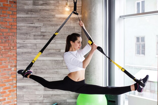 Fit young woman does stretching, push up and pull up on the gymnastics rings in gym