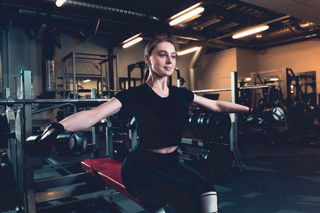 Fit young woman doing exercise with dumbbell in fitness center