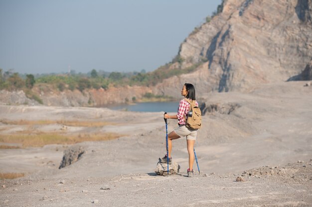 fit young woman hiking in the mountains standing on a rocky summit ridge with backpack and pole looking out over landscape.