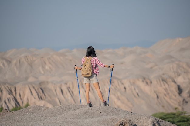 岩だらけの頂上の尾根に立っている山でハイキングする若い女性にぴったりです。バックパックとポールで風景を見渡せます。