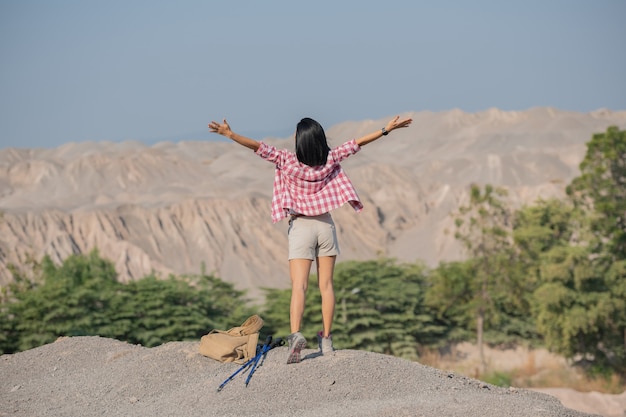 fit young woman hiking in the mountains standing on a rocky summit ridge with backpack and pole looking out over landscape.