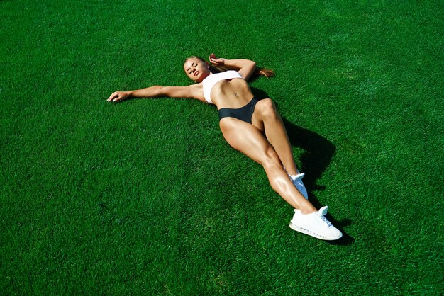 スタジアムのフィールドで草の上に横たわっている若い女性に合う