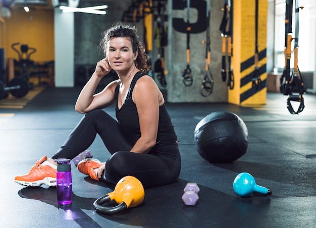 Fit young woman sitting on floor near exercise equipments in gym