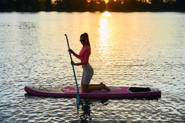 Подходит молодая женщина, занимающаяся серфингом на доске с веслом во время заката